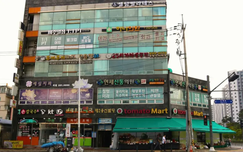 도심 번화가에 병원, 마트, 식당 등 여러 상업 시설 간판이 빼곡한 상가 건물이 보인다. 상가권리금 임대료 감정평가를 떠올리게 하는 복합적인 상권의 활기찬 모습이다.