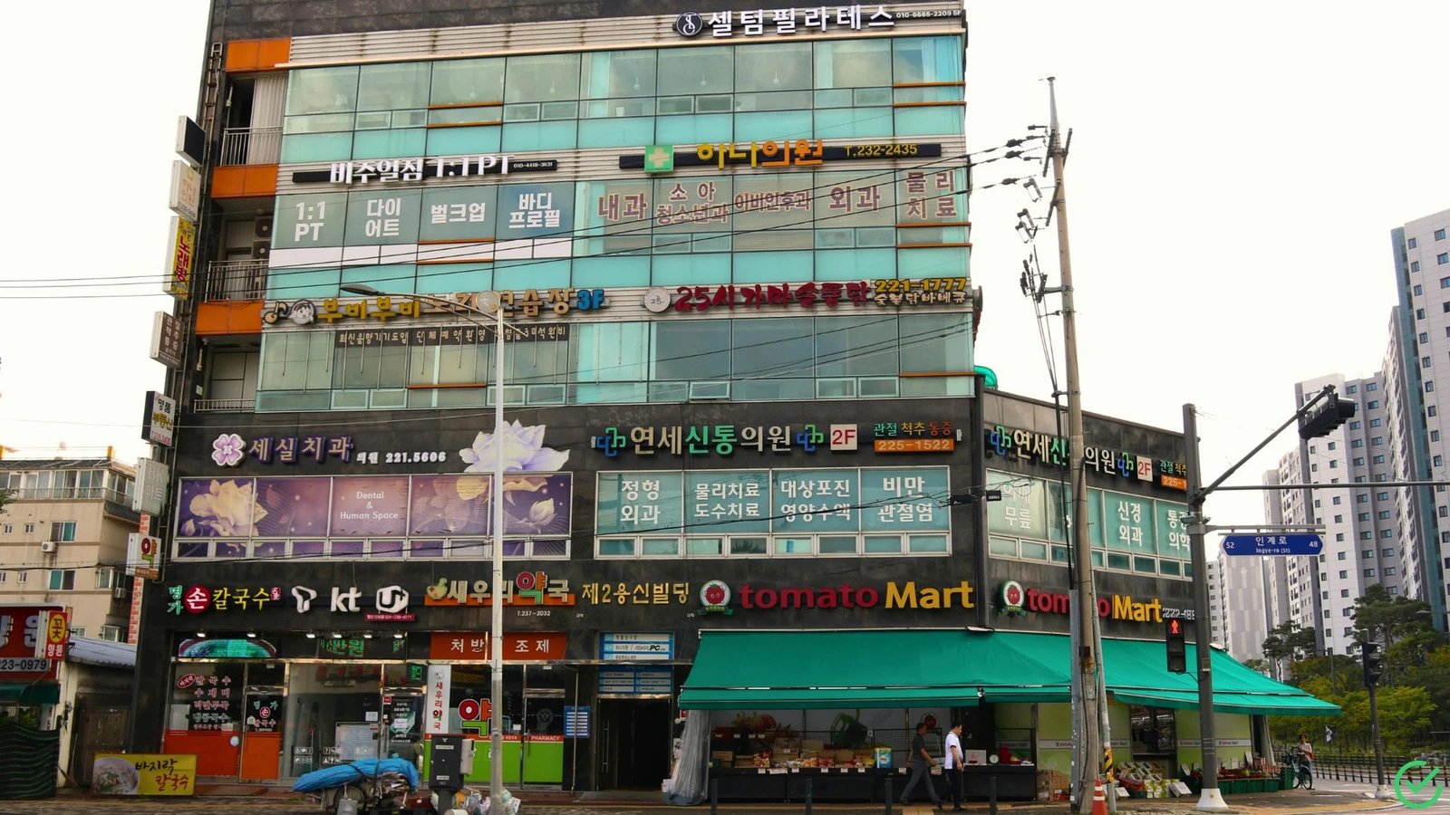 도심 번화가에 병원, 마트, 식당 등 여러 상업 시설 간판이 빼곡한 상가 건물이 보인다. 상가권리금 임대료 감정평가를 떠올리게 하는 복합적인 상권의 활기찬 모습이다.